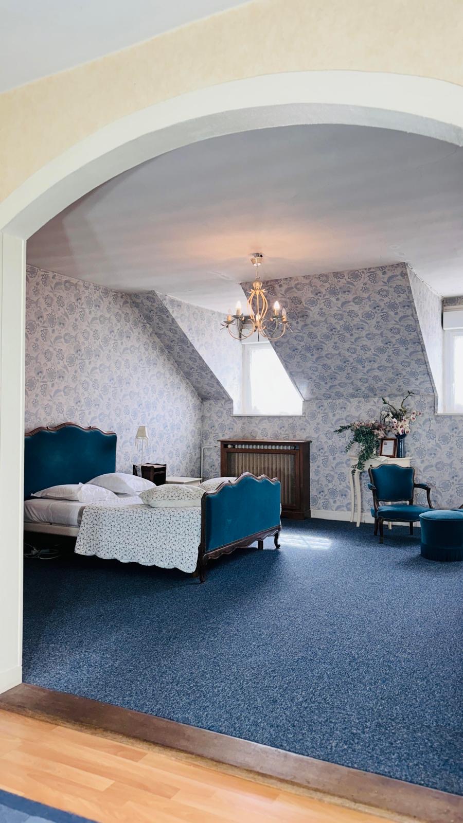 Grande chambre bleue avec lit ancien et papier peint fleuri